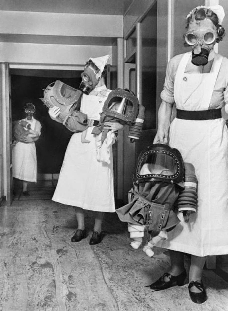 Nurses in gas-masks carry children inside the baby/toddler gas-mask